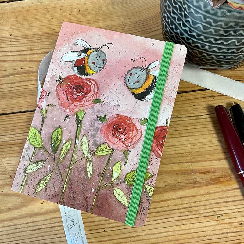 Alex Clark Bees & Roses Small Chunky Notebook on a wooden table with pens